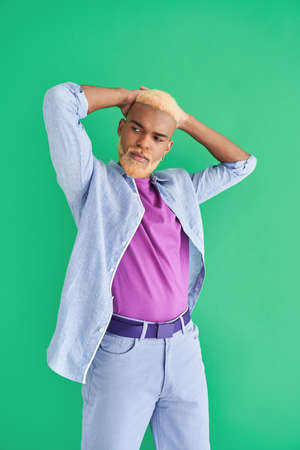 Guy with blonde hair looking away and touching his head with his hands while posingの写真素材