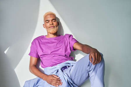 Multiracial man leaning at the white wall and resting with closed eyesの写真素材