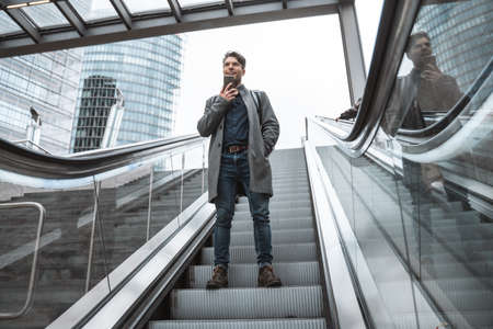 Businessman standing at the escalator with mobile phone and sending voice messageの写真素材