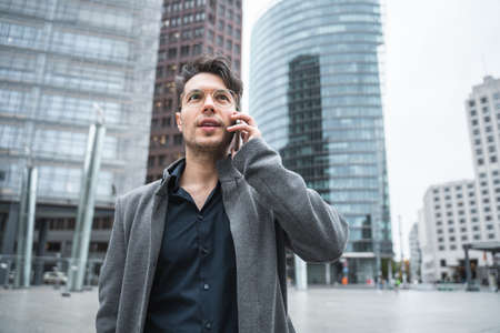 Serene man telling by mobile while walking with baggage along the cityの写真素材