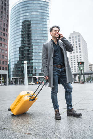 Businessman talking on the phone while standing with luggage at the streetの写真素材