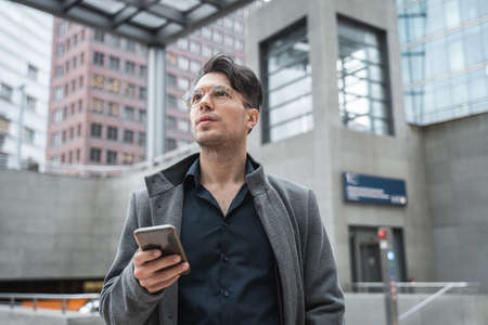 Handsome man holding cellphone while waiting for somebody at the streetの写真素材