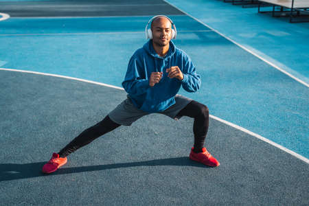 Positive man wearing headphones stretching body while doing exercise on open airの写真素材