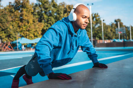 Sportive man standing in plank position on stadium running track and listening music