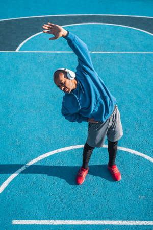 Smiling male athlete in wireless headphones doing workout on stadium