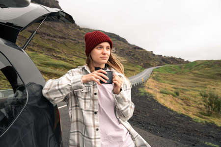 Woman traveler drinking hot tea and relaxing at the road near the mountainsの写真素材