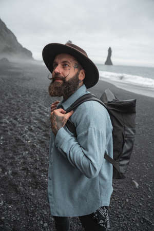 Tattooed man looking at the nature while walking with backpack through the seashore