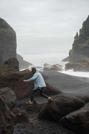 Man jumping at the rocks with moss and exploring nature of the Iceland beach