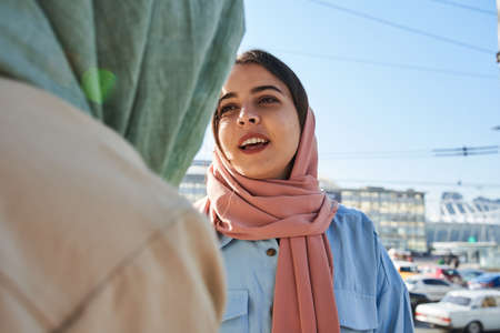 Friendly arabian girl wearing hijab chatting with her female best friend while walkingの写真素材