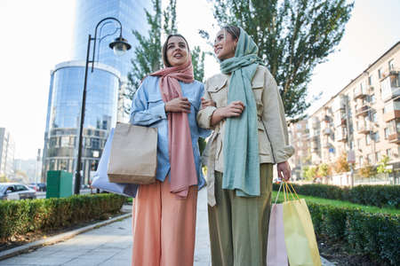 Two female muslim shopaholics walking through the street after great shopping