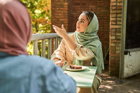 Multiracial girl in headscarf pointing at something while getting her friends attention