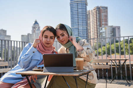 Arabian women wearing abayas sitting with coffee at cafeteria and looking at the tabletの写真素材