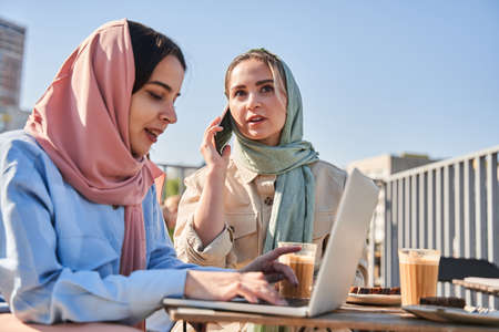 Concentrated islamic girl texting at the laptop keyboard while working at the cafeteriaの写真素材