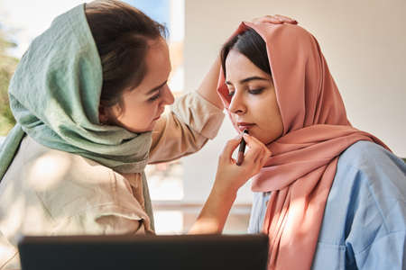 Arabic woman painting lips to her best friend wearing abaya while sitting at the cafeの写真素材