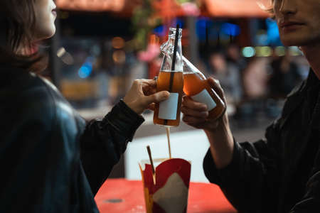 Man and woman clinking with bottles with beverages while sitting at the table