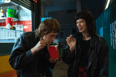 Girl laughing out loud and smoking cannabis cigarette while her boyfriend eating noodles