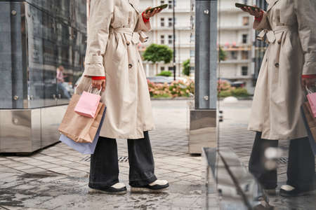 Woman holding shopping bags and her smartphone while shooting something at the cityの写真素材