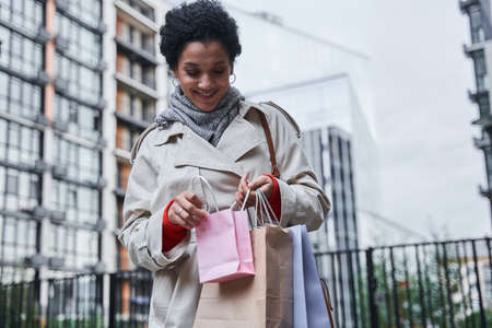 Stylish girl holding different shopping bags and looking inside with pleasure smileの写真素材