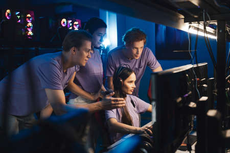 Two guys and girl at the computer club giving support to their friend during her game