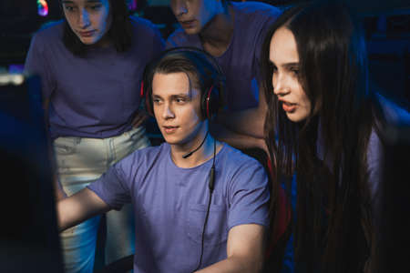 Boy playing in a computer club, while his friends standing behind and prompting