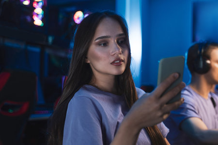 Woman looking at smartphone while sitting at internet cafe during the online tournamentの写真素材