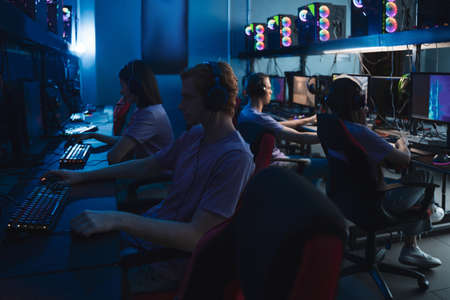 Group of young gamers in headsets playing in video games at the club
