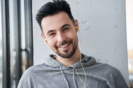 Man wearing earphones looking at the camera with happy smile while listening music at homeの写真素材