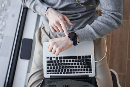 Man sitting at the windowsill and typing at the smartwatch while checking time at home
