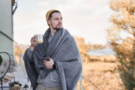 Man standing at the balcony and drinking hot beverage while spending time at the street