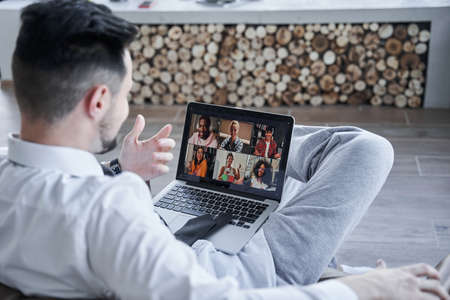 Businessman using laptop computer while having zoom call with his colleagues