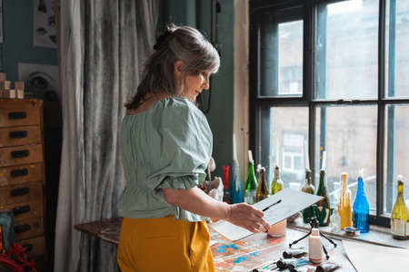 Senior lady comes up with a picture while working at her studio at the sunny dayの写真素材