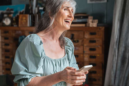 Overjoyed grey haired woman holding her smartphone and laughing out loud