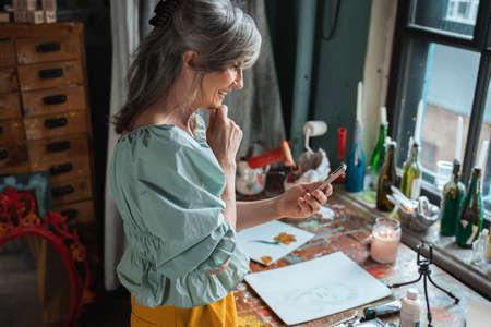 Woman evaluates something while looking at the screen of her mobile device with light smileの写真素材