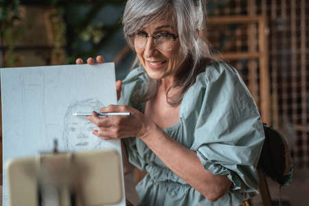 Artist holding pencil and showing something at her drawing while teaching