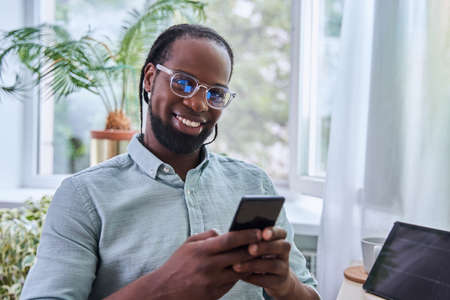 Bearded male wearing glasses typing message on smartphone while sitting
