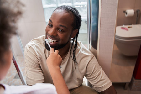 Man in domestic clothes looking at his little daughter while she cleaning his toothの写真素材