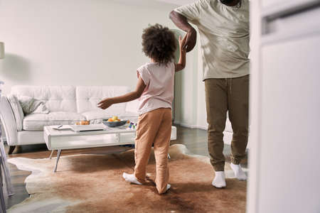 Father having fun and teaching his teenage kid to dance in modern living roomの写真素材