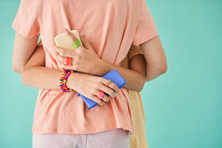 Unrecognizable girl embracing her bestie and holding two smartphones at the each hands