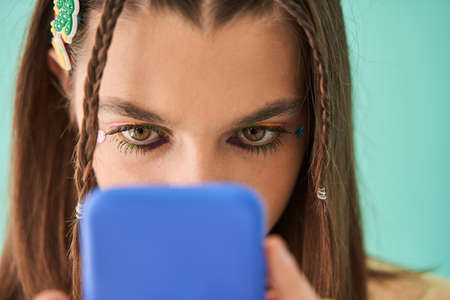 Caucasian teen girl with bright makeup looking at the cell phone and feeling involved