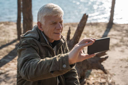 Man making selfie at his smartphone with water surface at the backgroundの写真素材