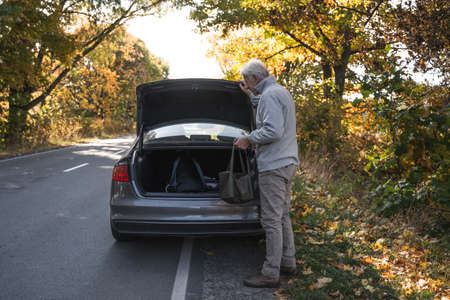 Man standing near his car with opened trunk and holding backpackの写真素材