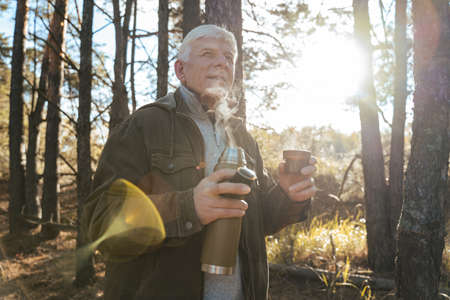 Man looking at the distance and drinking hot tea while relaxing after walkingの写真素材