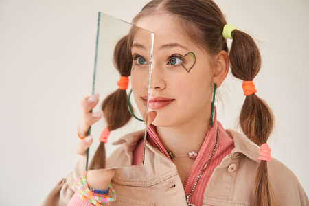 Girl with creative hairstyle playing with mirror and having fun during the shootingの写真素材