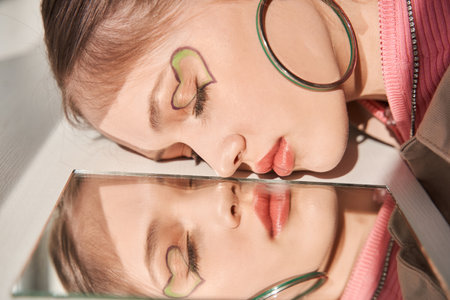 Calm girl with bright and creative makeup laying at the floor and reflecting at the mirrorの写真素材