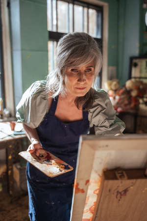 Creative woman having fun with paint and brush while standing in front of the easelの写真素材