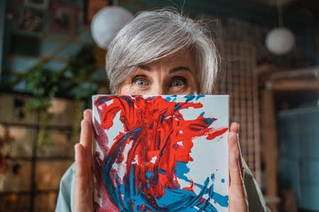 Female artist hiding her face behind her picture and showing positive emotionsの写真素材