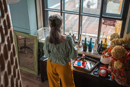 Mature woman enjoying favorite beverage while standing in front of the window and relaxingの写真素材
