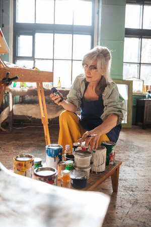 Elderly woman choosing paints while preparing painting at home