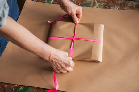 Mature woman wrapping gift with craft wrapping paper in her art room at the tableの写真素材