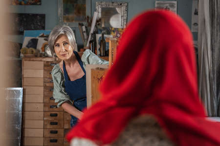 Grey haired woman painting girl model sitting on chair and posing for creative workshopの写真素材